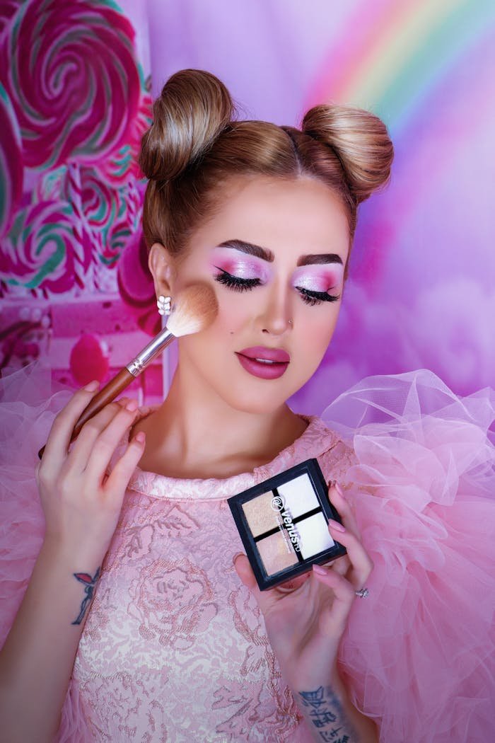 creative-02 Vibrant portrait of a woman applying makeup with a pink theme and elegant hairstyle.